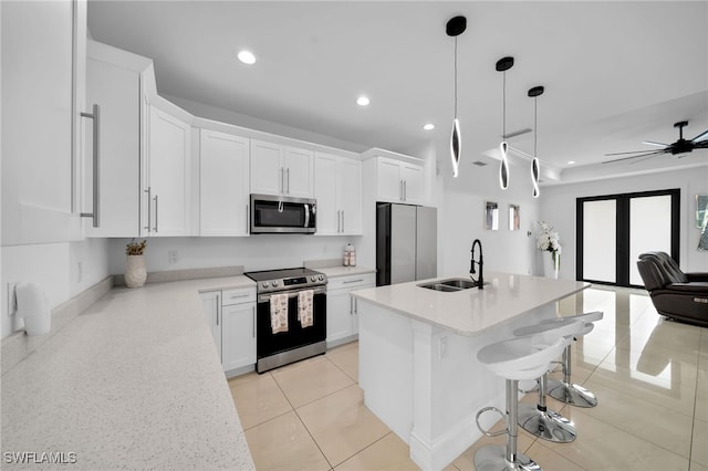 kitchen featuring appliances with stainless steel finishes, white cabinetry, ceiling fan, a center island with sink, and sink