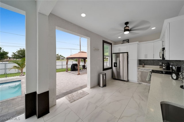 kitchen featuring ceiling fan, light stone counters, backsplash, white cabinetry, and appliances with stainless steel finishes