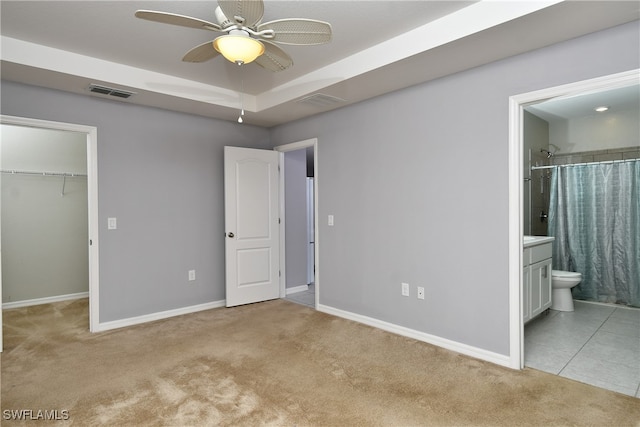 unfurnished bedroom featuring a closet, light carpet, connected bathroom, a walk in closet, and ceiling fan