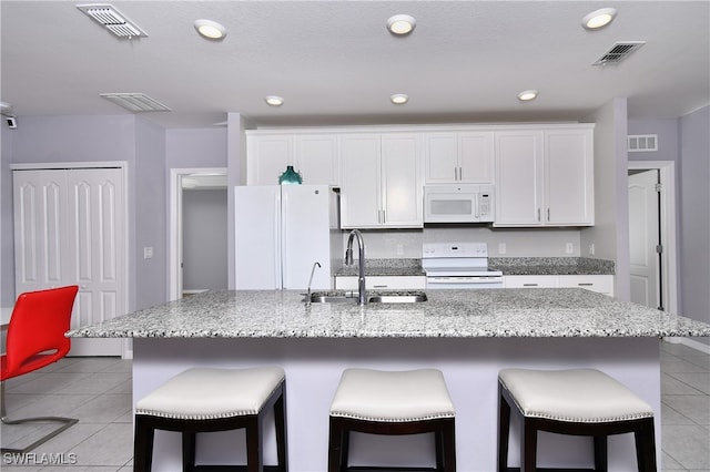 kitchen with an island with sink, sink, white appliances, and white cabinetry