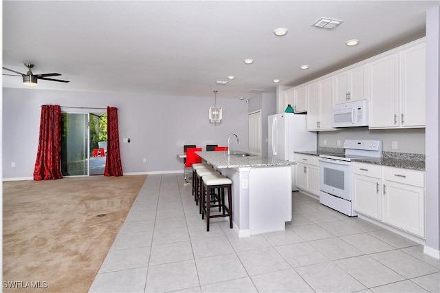 kitchen with ceiling fan, an island with sink, white appliances, a kitchen breakfast bar, and light colored carpet