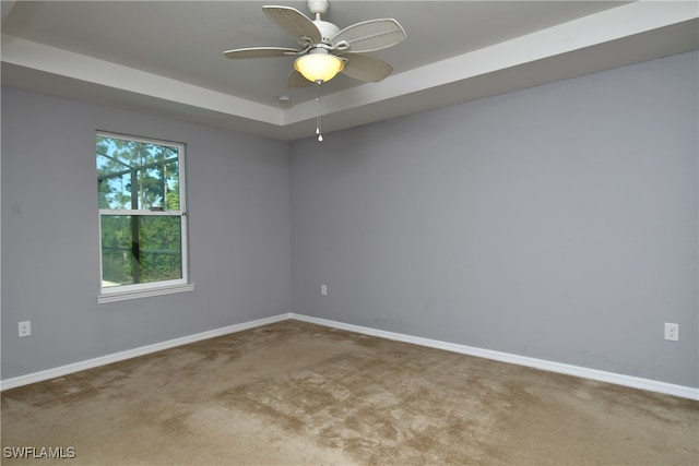 carpeted empty room featuring ceiling fan and a raised ceiling