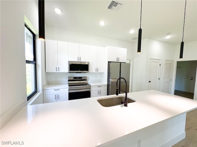 kitchen with stainless steel appliances, hanging light fixtures, sink, and white cabinetry