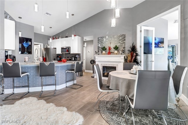 dining space with sink, a fireplace, light hardwood / wood-style floors, and high vaulted ceiling