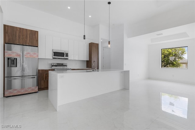 kitchen featuring hanging light fixtures, white cabinetry, an island with sink, stainless steel appliances, and sink