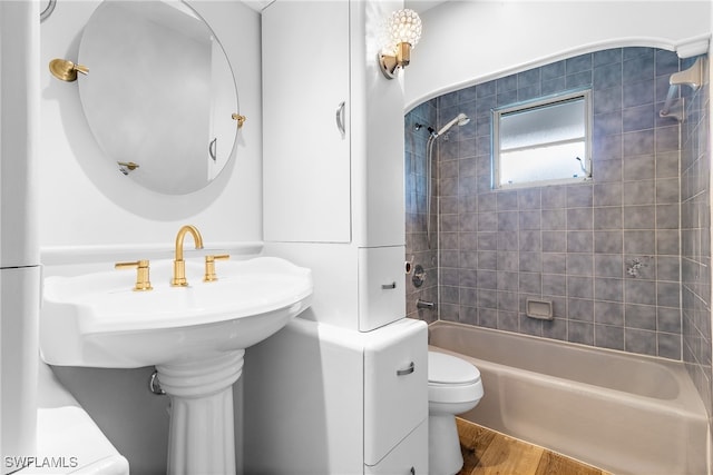 bathroom with wood-type flooring, tiled shower / bath, and toilet