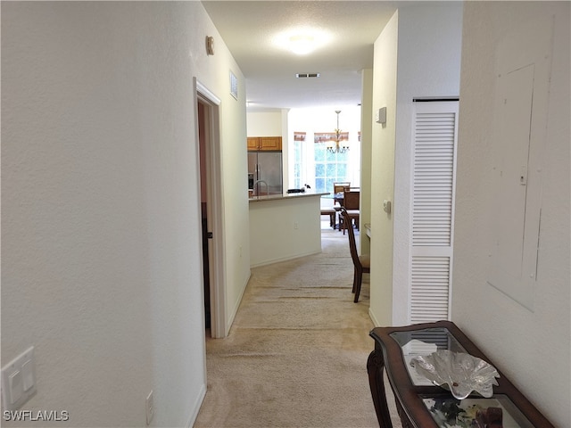 corridor featuring light carpet, a notable chandelier, and a textured ceiling