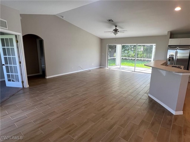 unfurnished living room featuring arched walkways, ceiling fan, lofted ceiling, baseboards, and wood tiled floor