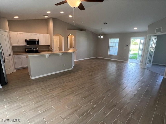 kitchen with stove, ceiling fan with notable chandelier, an island with sink, white cabinetry, and a breakfast bar area