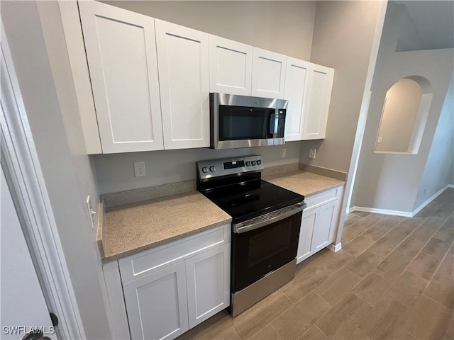 kitchen with light countertops, electric range, stainless steel microwave, and white cabinetry