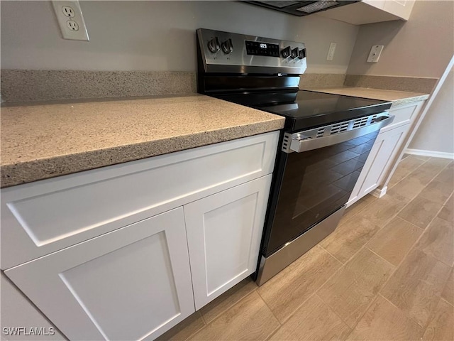 kitchen featuring electric range, wood finish floors, light stone counters, and white cabinets