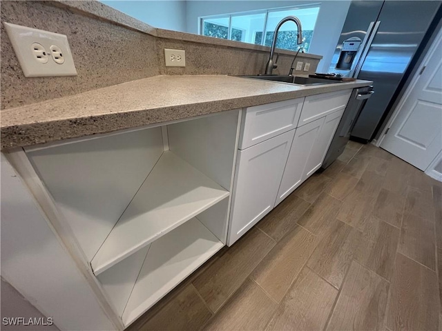 kitchen featuring light stone counters, white cabinets, a sink, and wood finished floors