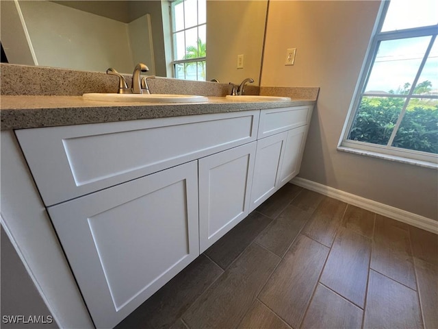 bathroom with double vanity, a sink, baseboards, and wood finished floors