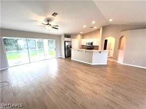 unfurnished living room featuring ceiling fan, wood finished floors, arched walkways, and lofted ceiling