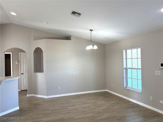 spare room with arched walkways, visible vents, vaulted ceiling, and wood finished floors