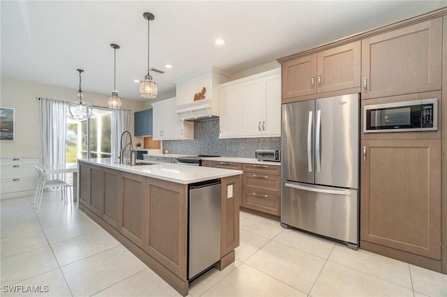 kitchen with a kitchen island with sink, sink, appliances with stainless steel finishes, tasteful backsplash, and decorative light fixtures