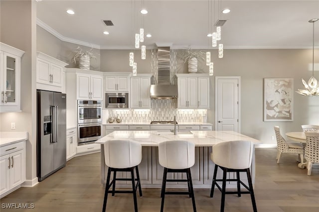 kitchen featuring a center island with sink, white cabinets, decorative light fixtures, and appliances with stainless steel finishes