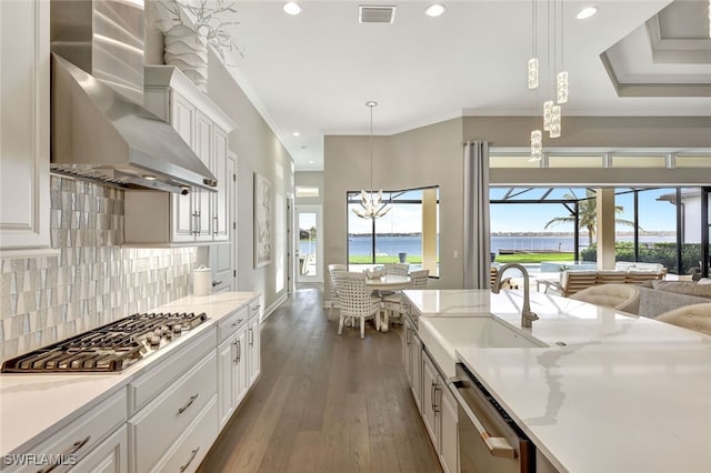 kitchen featuring pendant lighting, sink, wall chimney exhaust hood, appliances with stainless steel finishes, and white cabinetry