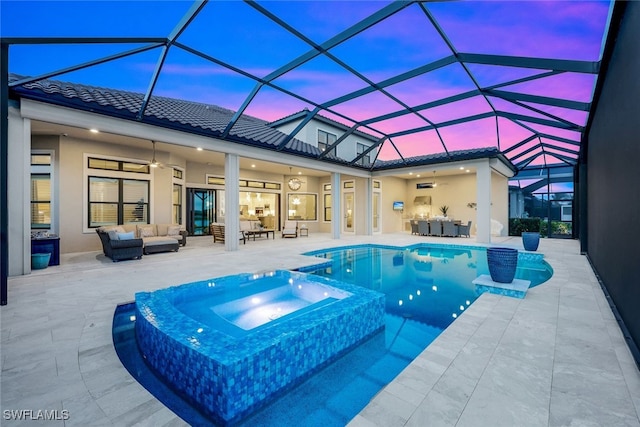 pool at dusk featuring a lanai, outdoor lounge area, ceiling fan, and an in ground hot tub