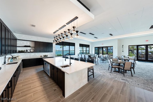 kitchen featuring light stone counters, sink, an island with sink, and hanging light fixtures