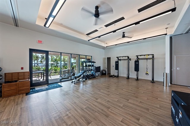 gym featuring a tray ceiling, ceiling fan, and hardwood / wood-style flooring