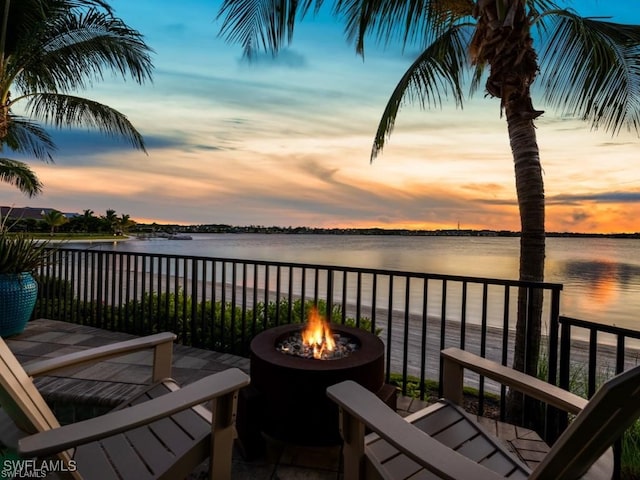 balcony at dusk featuring an outdoor fire pit and a water view