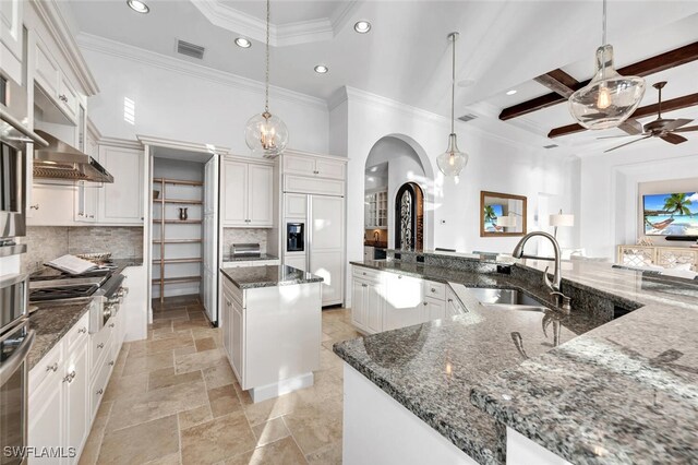 kitchen featuring sink, decorative light fixtures, dark stone countertops, backsplash, and a large island with sink