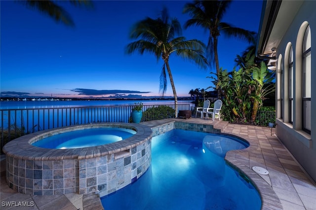 pool at dusk with a patio, an in ground hot tub, and a water view