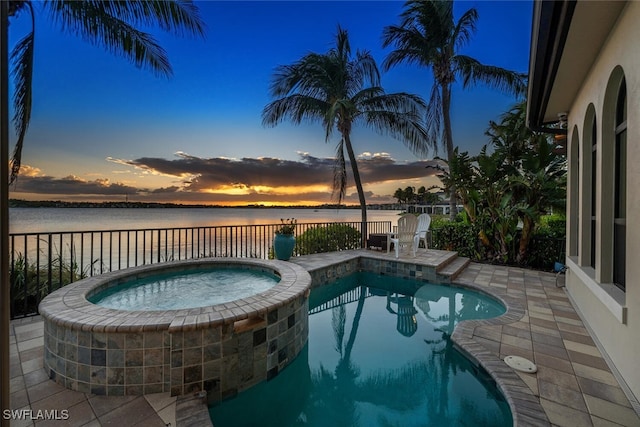 pool at dusk featuring an in ground hot tub and a water view