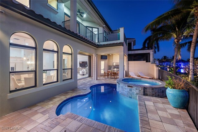 pool at night featuring an in ground hot tub and a patio