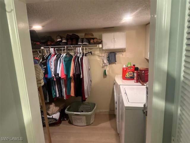 washroom with light wood-type flooring, a textured ceiling, washer and dryer, and cabinets