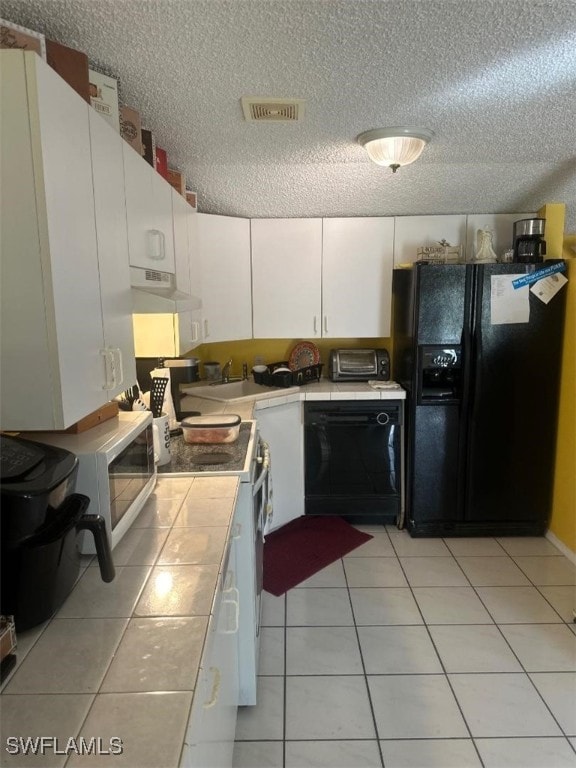 kitchen with a textured ceiling, black appliances, light tile patterned floors, and white cabinets