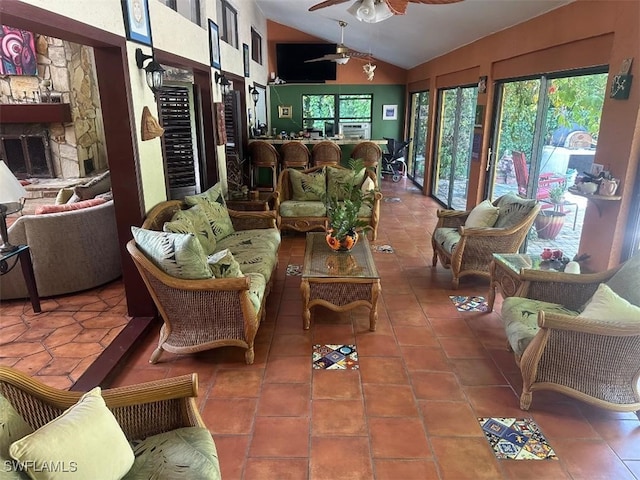 sunroom featuring ceiling fan, a stone fireplace, plenty of natural light, and vaulted ceiling