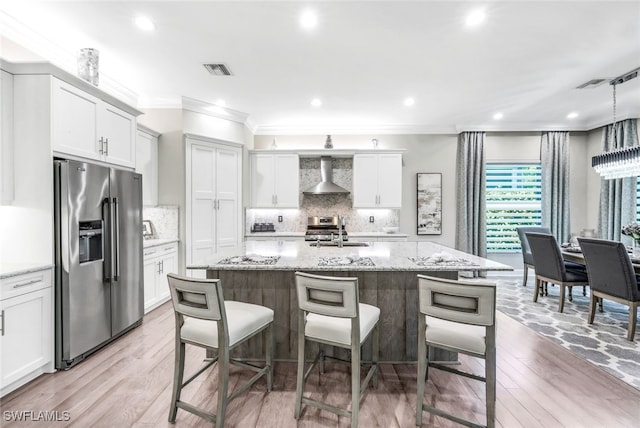 kitchen with white cabinetry, an island with sink, wall chimney exhaust hood, and appliances with stainless steel finishes