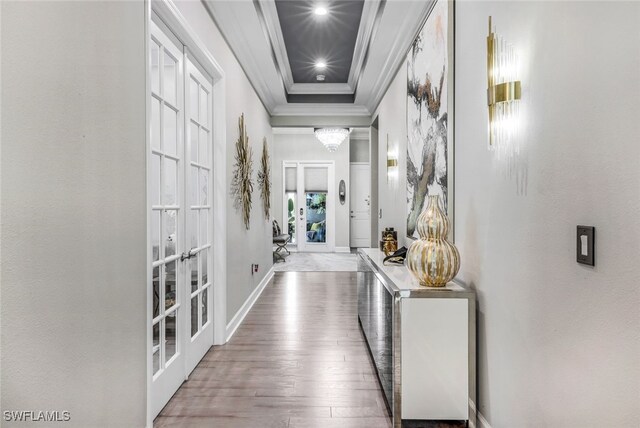 hall with a tray ceiling, wood-type flooring, ornamental molding, and french doors