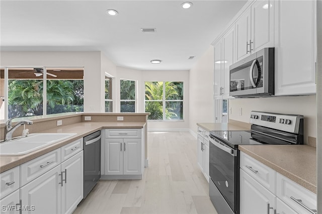 kitchen with appliances with stainless steel finishes, sink, light hardwood / wood-style flooring, and white cabinets