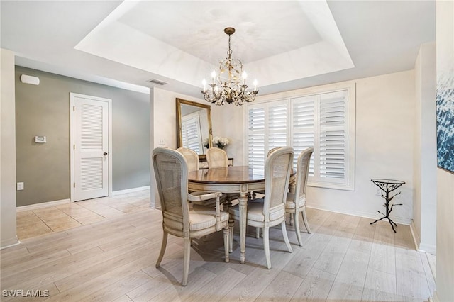 dining space with an inviting chandelier, a tray ceiling, and light hardwood / wood-style flooring