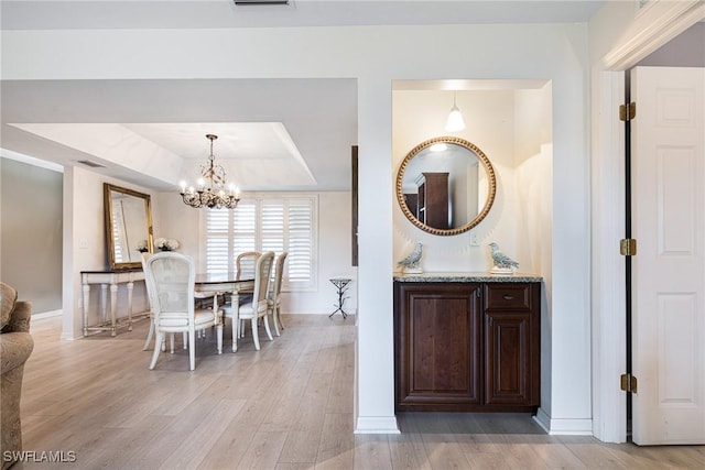 dining area with a raised ceiling, a chandelier, and light hardwood / wood-style flooring