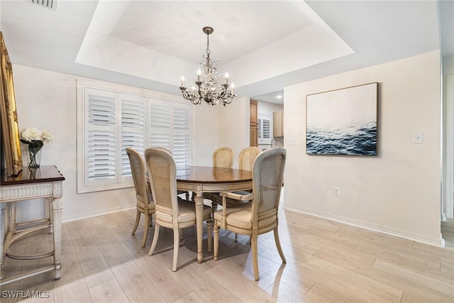 dining space with a raised ceiling, a chandelier, and light wood-type flooring