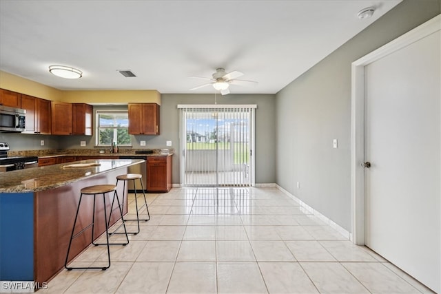 kitchen with ceiling fan, appliances with stainless steel finishes, light tile patterned floors, and dark stone counters