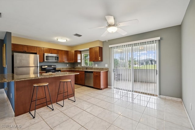 kitchen with appliances with stainless steel finishes, a breakfast bar, a center island, ceiling fan, and sink