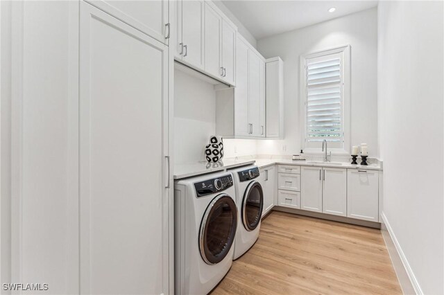 clothes washing area featuring sink, washer and clothes dryer, cabinets, and light wood-type flooring