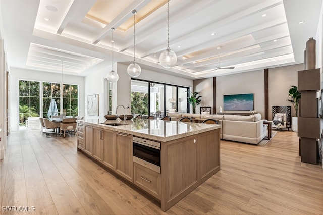 kitchen with light stone countertops, sink, hanging light fixtures, light hardwood / wood-style floors, and a kitchen island with sink