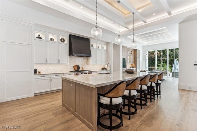 kitchen featuring light stone countertops, light wood-type flooring, premium range hood, white cabinets, and a large island