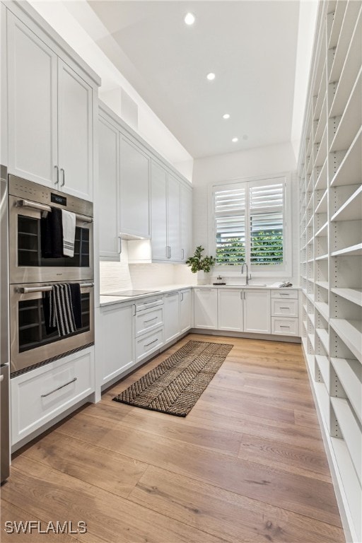 kitchen featuring white cabinetry, sink, double oven, light hardwood / wood-style floors, and black electric cooktop