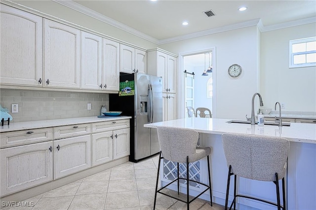 kitchen featuring backsplash, stainless steel fridge, ornamental molding, light tile patterned floors, and a breakfast bar area