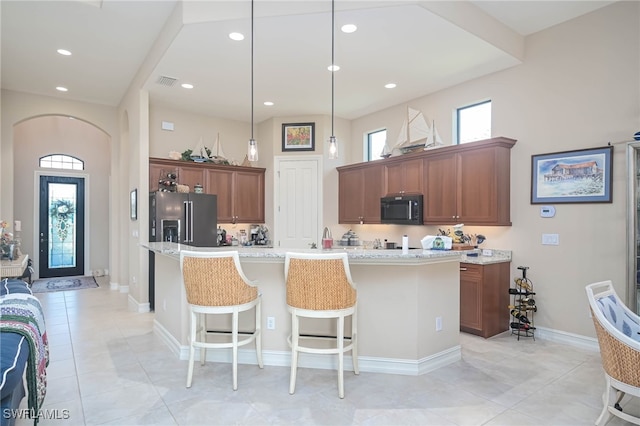 kitchen with light stone countertops, an island with sink, decorative light fixtures, and high end refrigerator