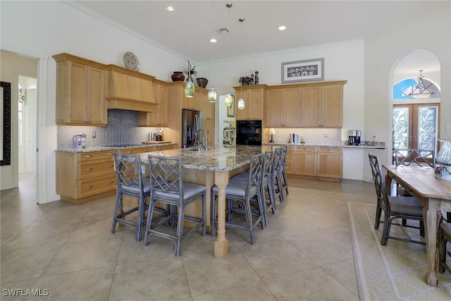 kitchen featuring light stone counters, an island with sink, stainless steel fridge, ornamental molding, and french doors