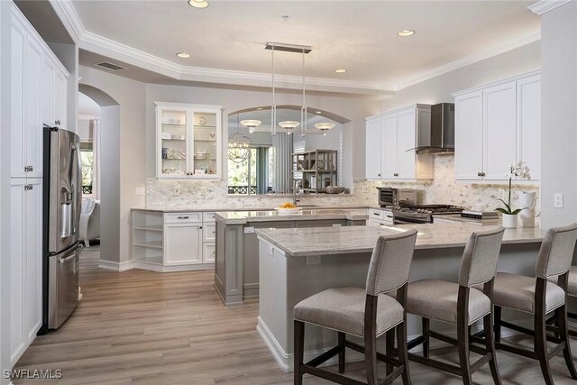 kitchen with a breakfast bar area, kitchen peninsula, wall chimney exhaust hood, appliances with stainless steel finishes, and a healthy amount of sunlight