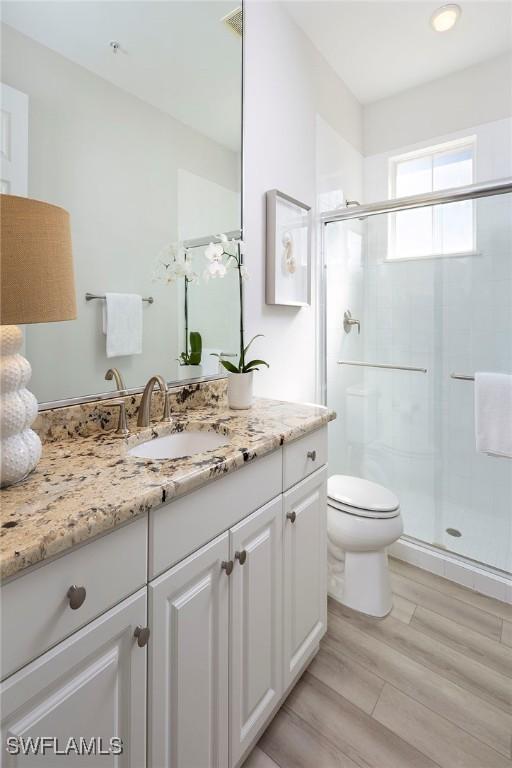 bathroom with wood-type flooring, walk in shower, vanity, and toilet